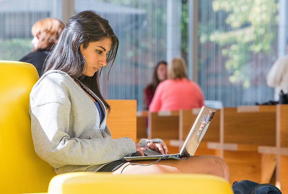 A female student working on a laptop while sitting on a couch A female student working on a laptop while sitting on a couch