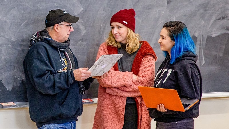 Dave Koranda holds a laptop and talks to two students