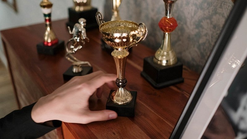 A hand reaching toward several trophies sitting on a dresser. A hand reaching toward several trophies sitting on a dresser.