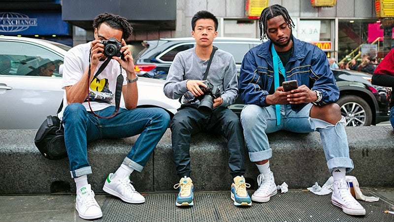 Three students in NYC sitting on curb holding cameras. Three students in NYC sitting on curb holding cameras.