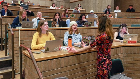 Whitney Phillips speaks to two students in a large classroom